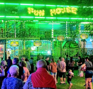 People crowd around a neon green fun house at a fair.