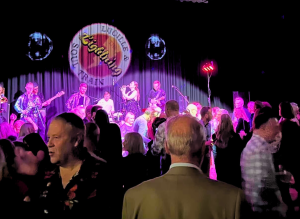 A band plays under purple lights as a crowd watches.