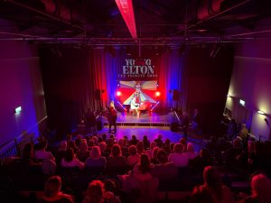 Audience in retractable seats watching a tribute act with theatre lighting 